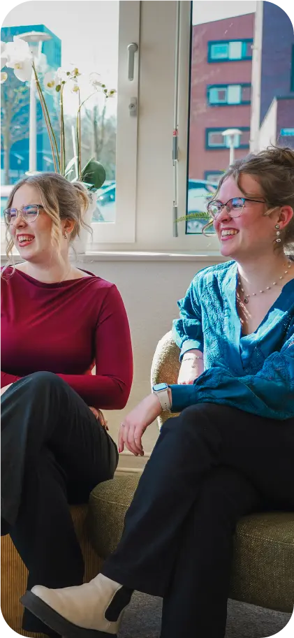 Twee collega's van VR-Innovations zitten lachend in gesprek bij het raam op kantoor